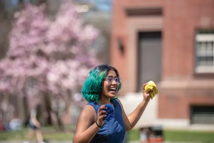 A student smiling and holding bean bags, while playing a lawn game.